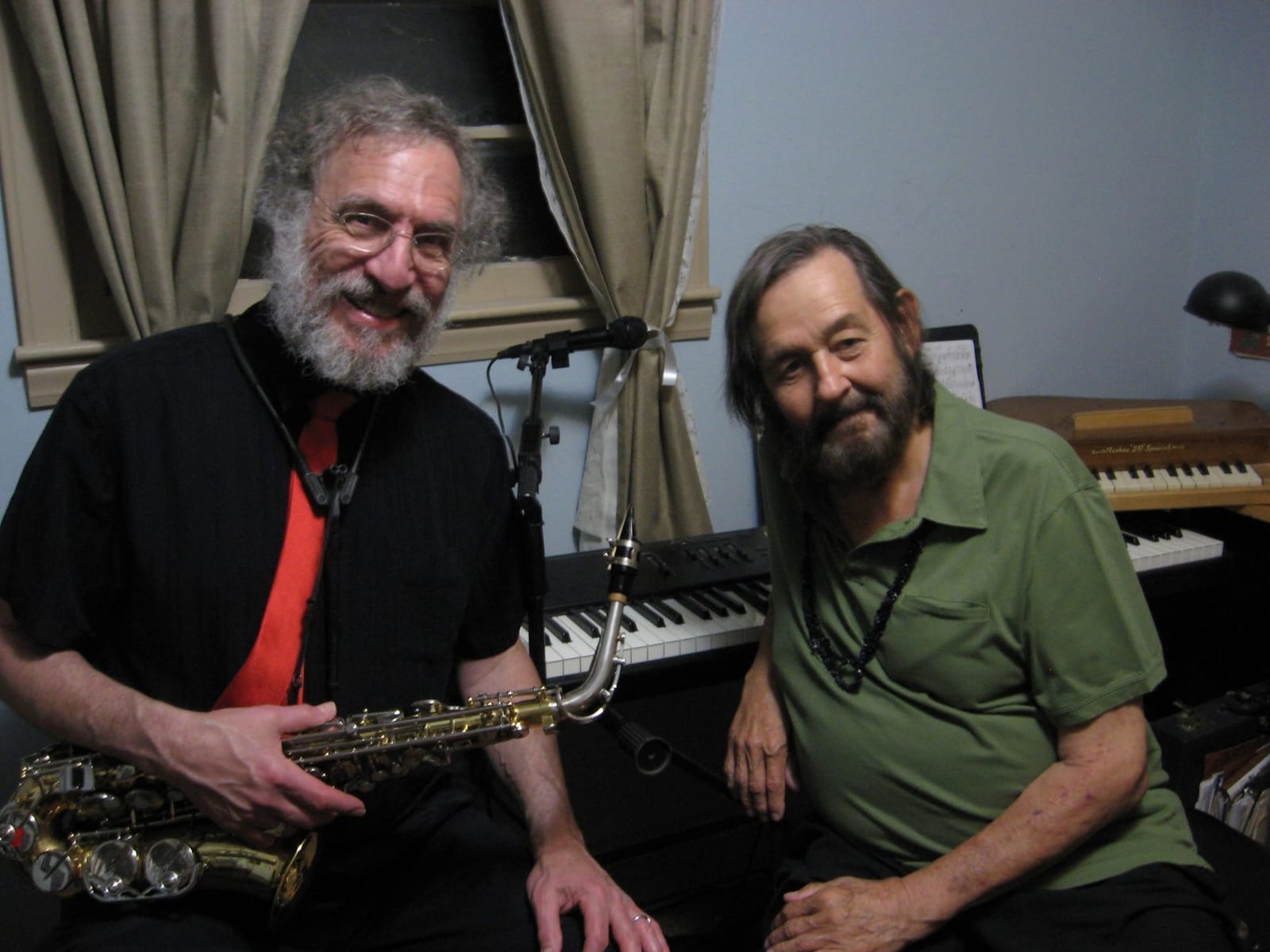 David Kreimer holding an alto sax and Marc Puricelli sitting beside a keyboard, both smiling at the camera.